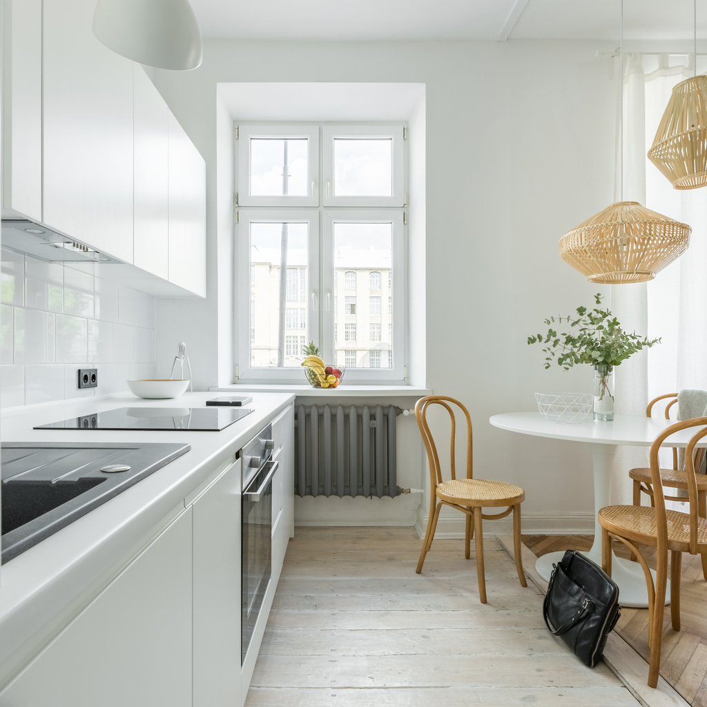 A modern white kitchen with table, chair, and a radiator. 